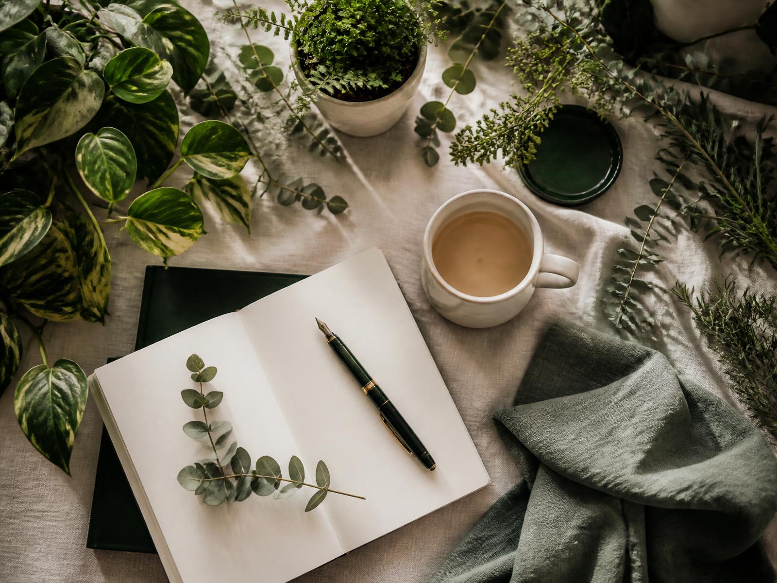 A calm flat lay of lush greenery, herbs, and an open planner on a cream linen surface.
